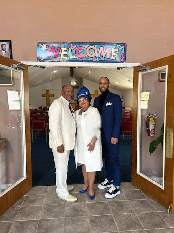 Church members smiling beneath the colorful Welcome sign at the church entrance