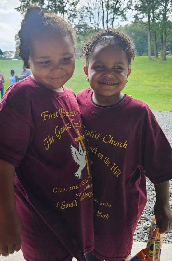 Ana and Karen's grandchild smiling in their church shirts at the park