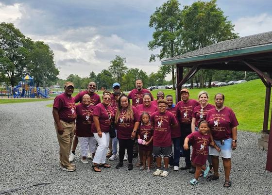 Church members in maroon church shirts gathered by the pavilion at the park
